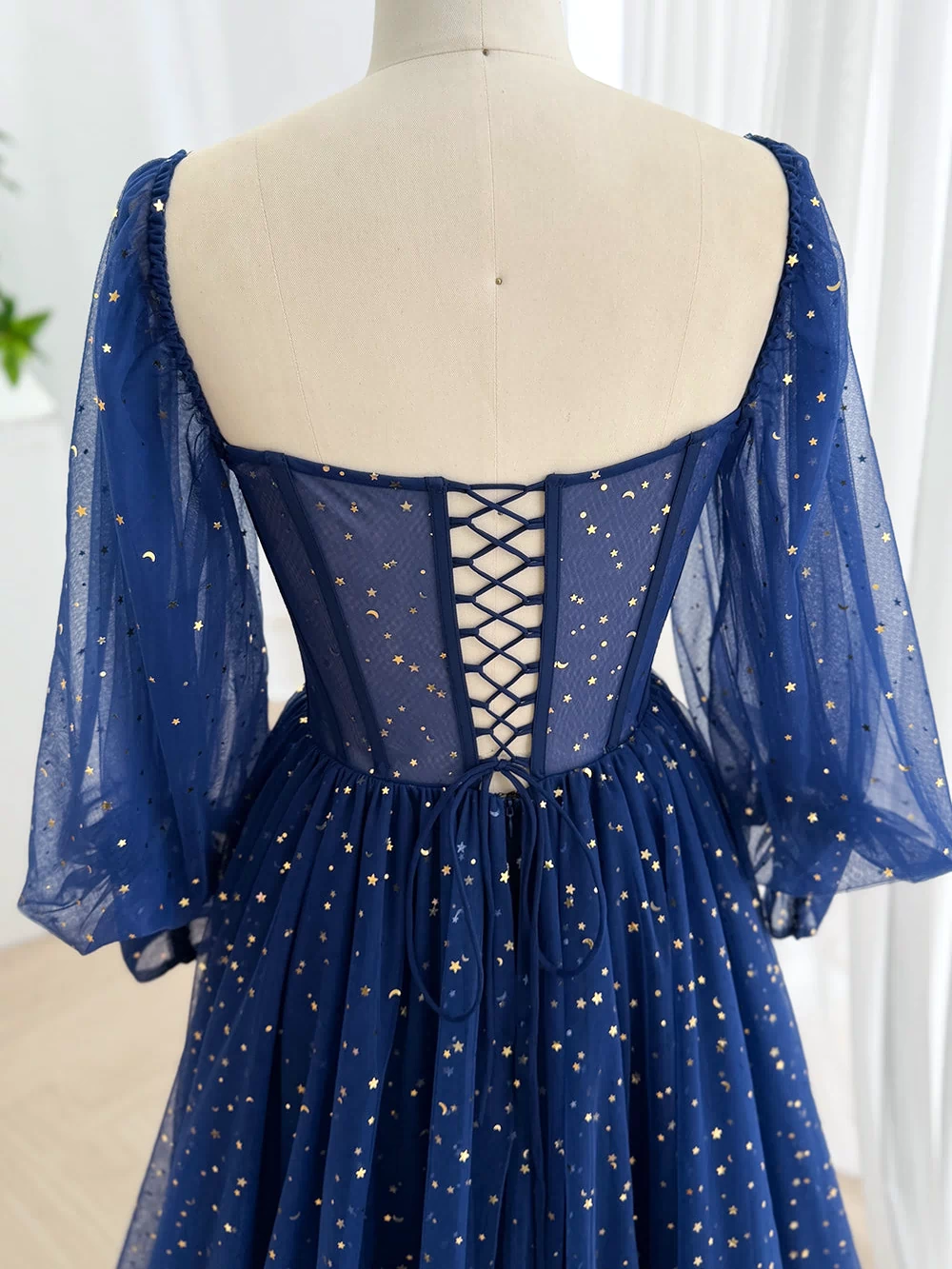 Rear view displays lace-up closure over sheer blue back, supportive boning, moon print bishop arms, romantic fit, airy charm.