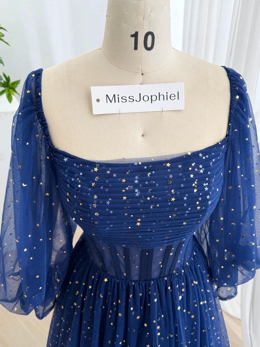 Detailed upper angle presents pleated bust, off-shoulder puff design, metallic motifs, elegant fantasy occasion look glamour.
