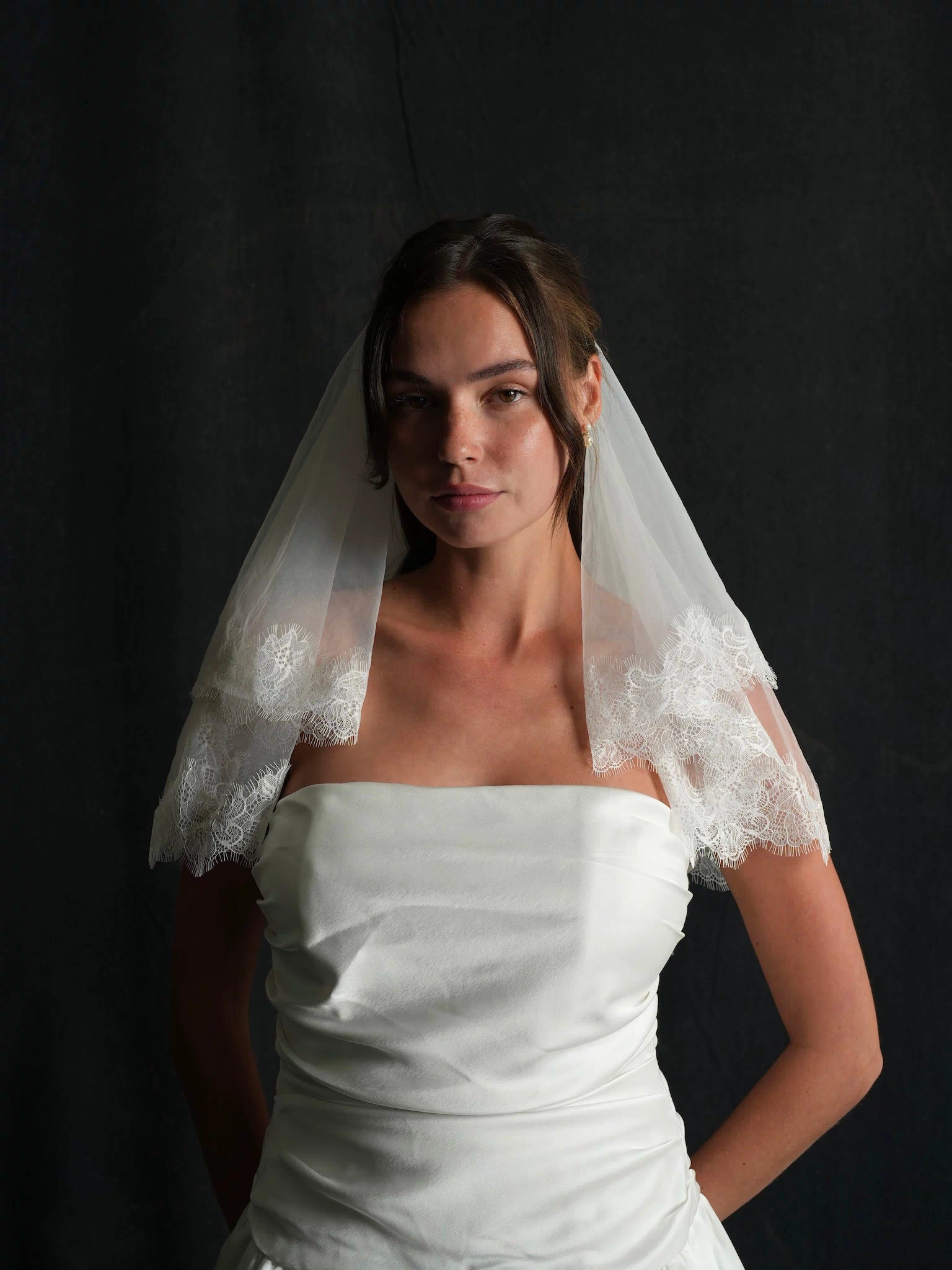 Woman wearing a white strapless dress and a chantilly lace short two tier bachelorette veil