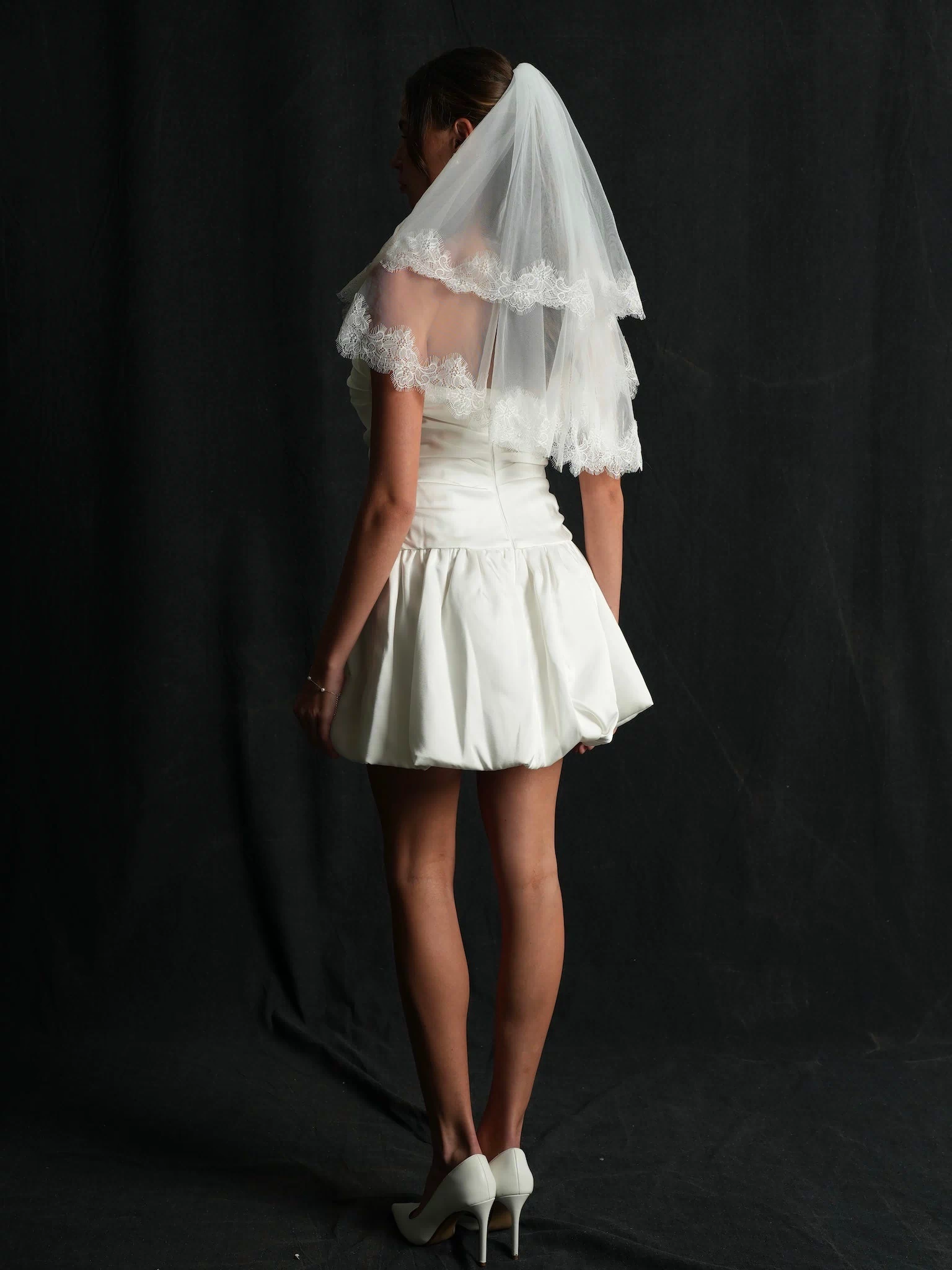 Woman wearing a white dress and mini chantilly lace short two tier bachelorette veil
