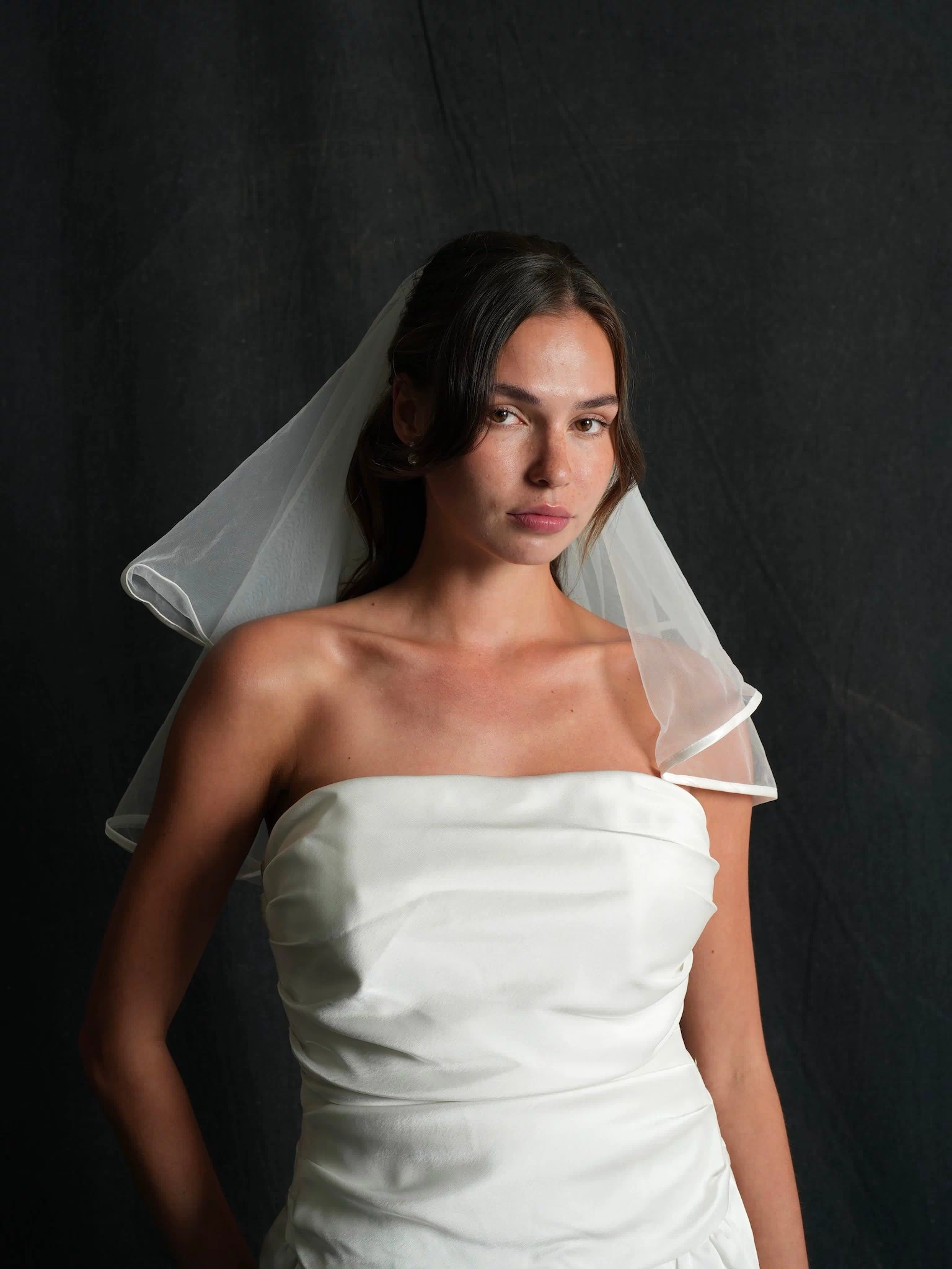 Woman wearing a mini satin short two tier bachelorette veil against a dark background