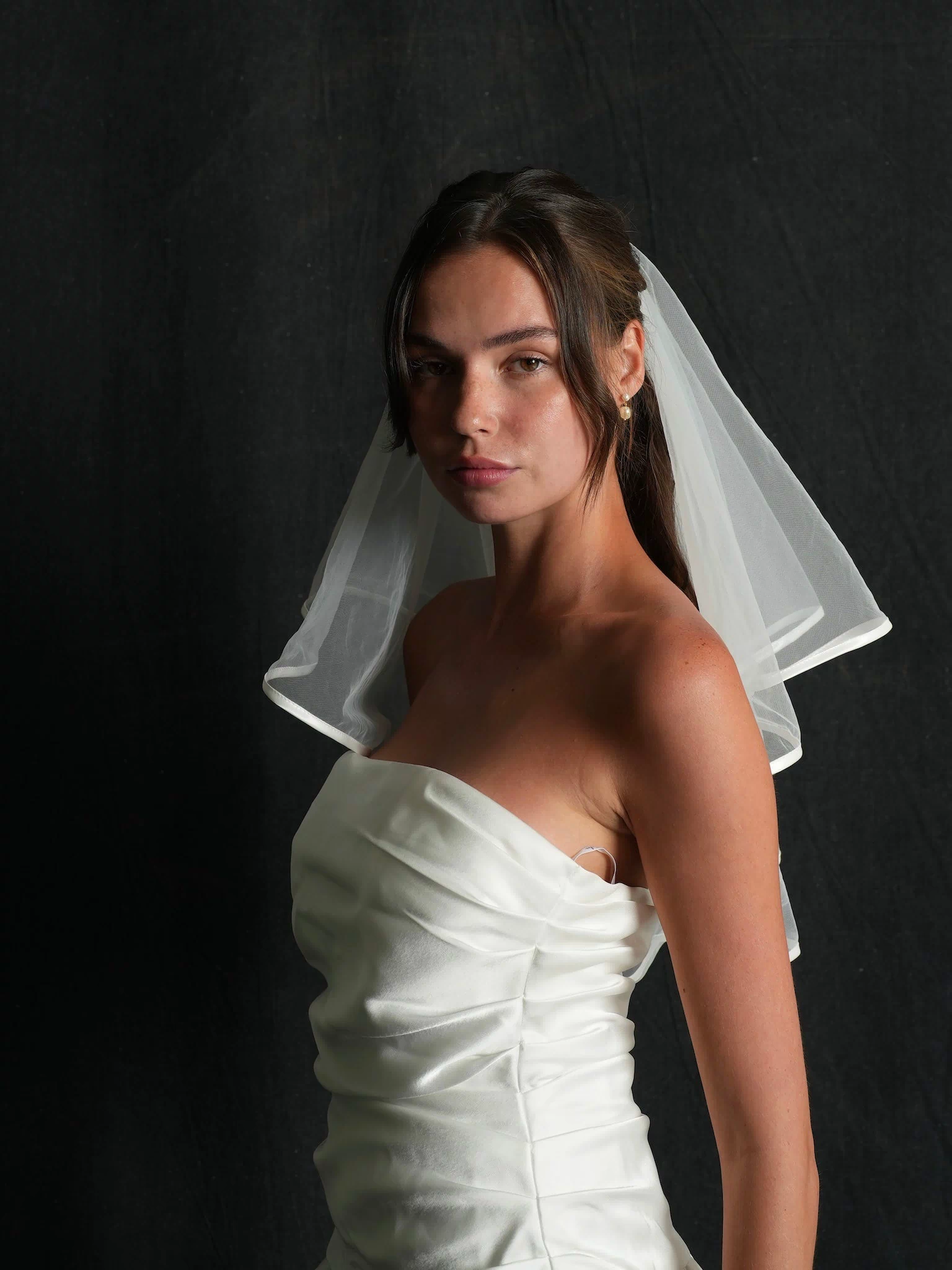 Woman wearing a mini short two tier bachelorette veil against a black background