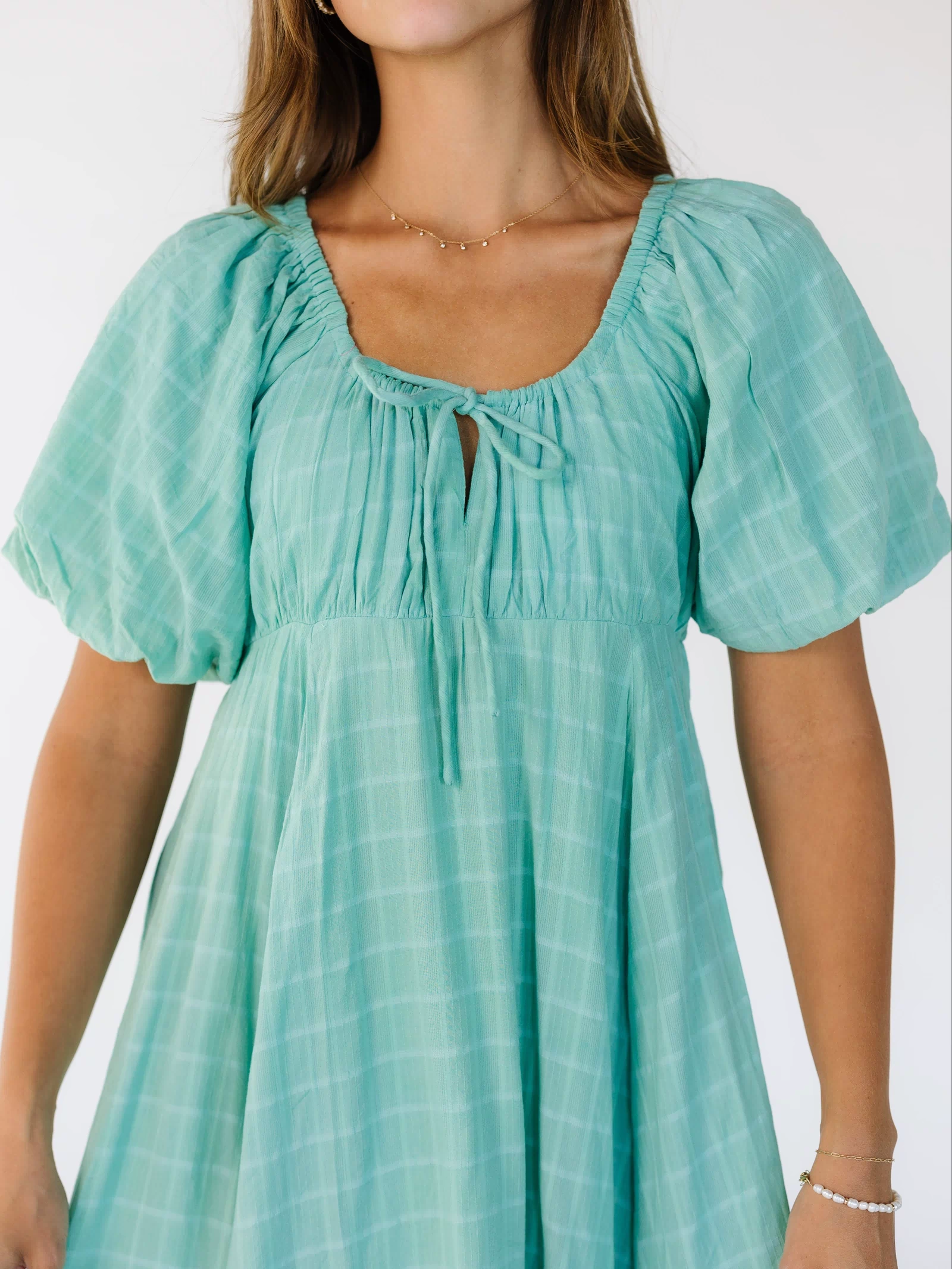 Close view of a young woman wearing a mint green dress with an empire waist, scoop neckline and short balloon sleeves.