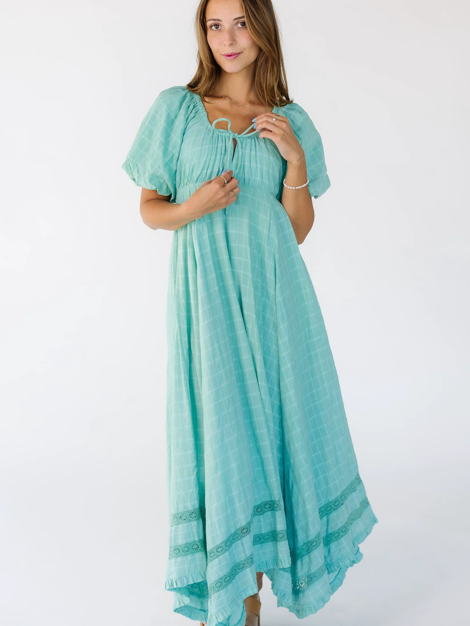 Young woman wearing a mint green midi-maxi dress with 2 rows of lace insets above the narrow ruffle hem with a scoop neckline.