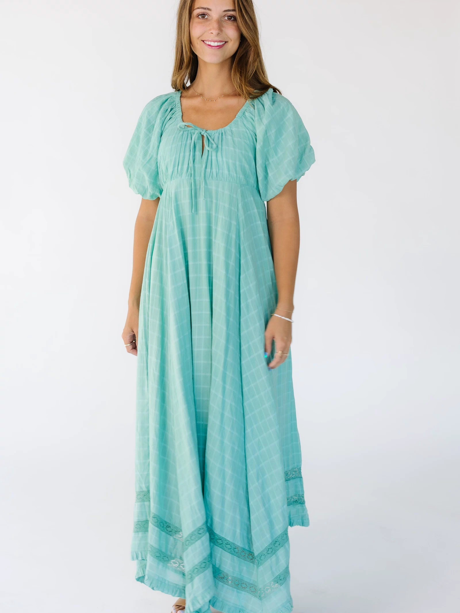 Woman wearing a mint green midi-maxi dress with a drawstring-scoop neckline, balloon sleeves and a loose fitting skirt.