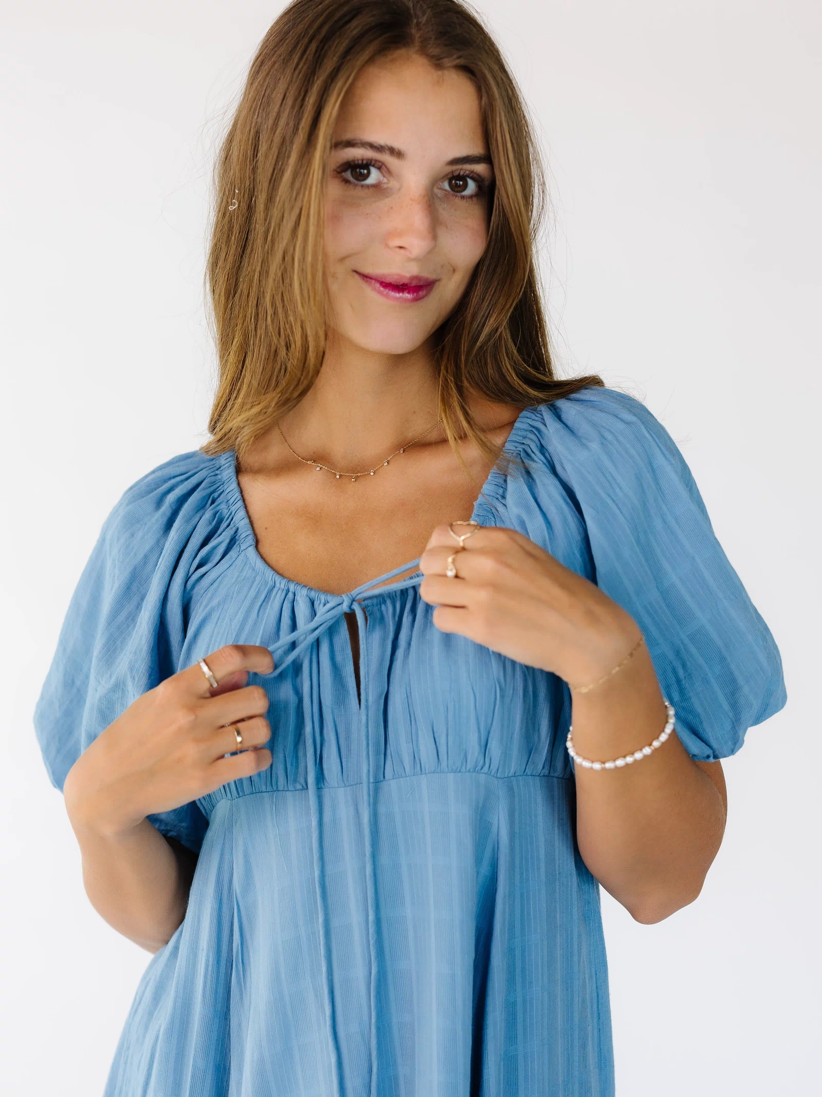 Close view of a woman wearing a blue dress with an empire waist, a drawstring-scoop neckline and balloon sleeves.