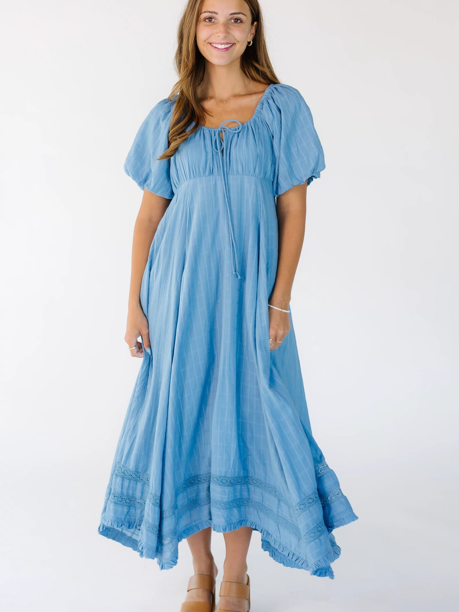 Young woman wearing a loose fitting, flowy midi-maxi dress in blue with an empire waist and balloon sleeves.