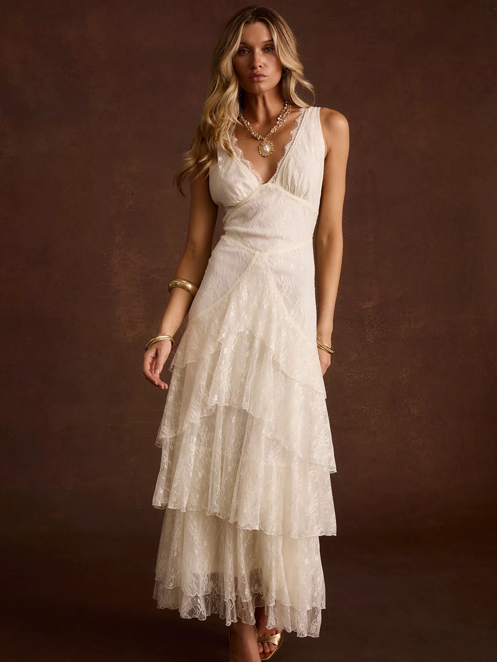 Cream lace maxi dress with V-neck and tiered ruffle skirt, styled with gold sandals.