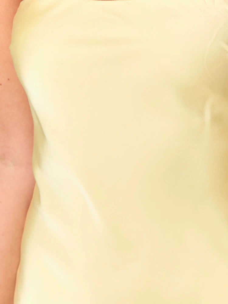 Close-up of the smooth yellow satin fabric of the strapless mini dress bodice