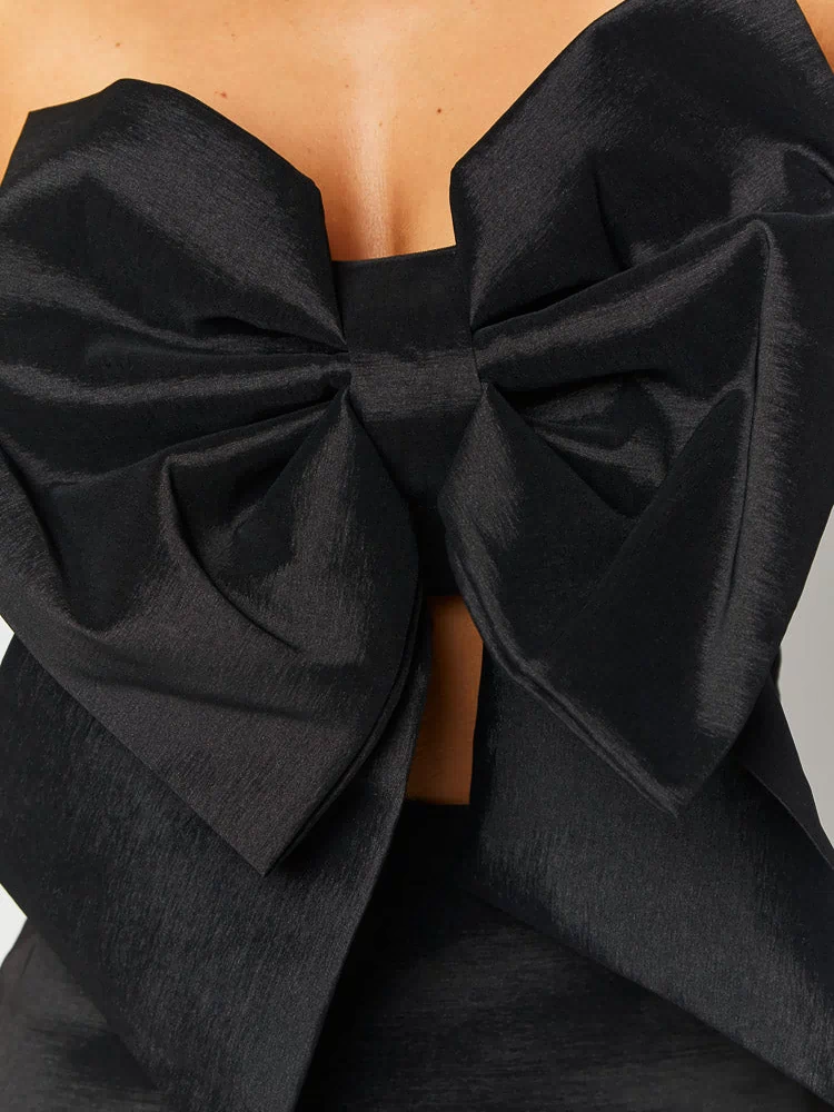 Close-up of the oversized black bow detail on a strapless mini dress, showing the textured fabric and a front cut-out