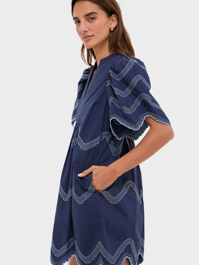 Woman models the Navy Embroidered Weston Mini Dress with classic scalloped trims and fluttery sleeves, embodying effortless, high-end style perfect for any fun occasion.