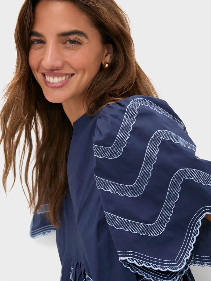 Woman in Navy Embroidered Weston Mini Dress with scalloped trim and gold hoops, embodying classic, effortless style; perfect for fun, high-end occasions.