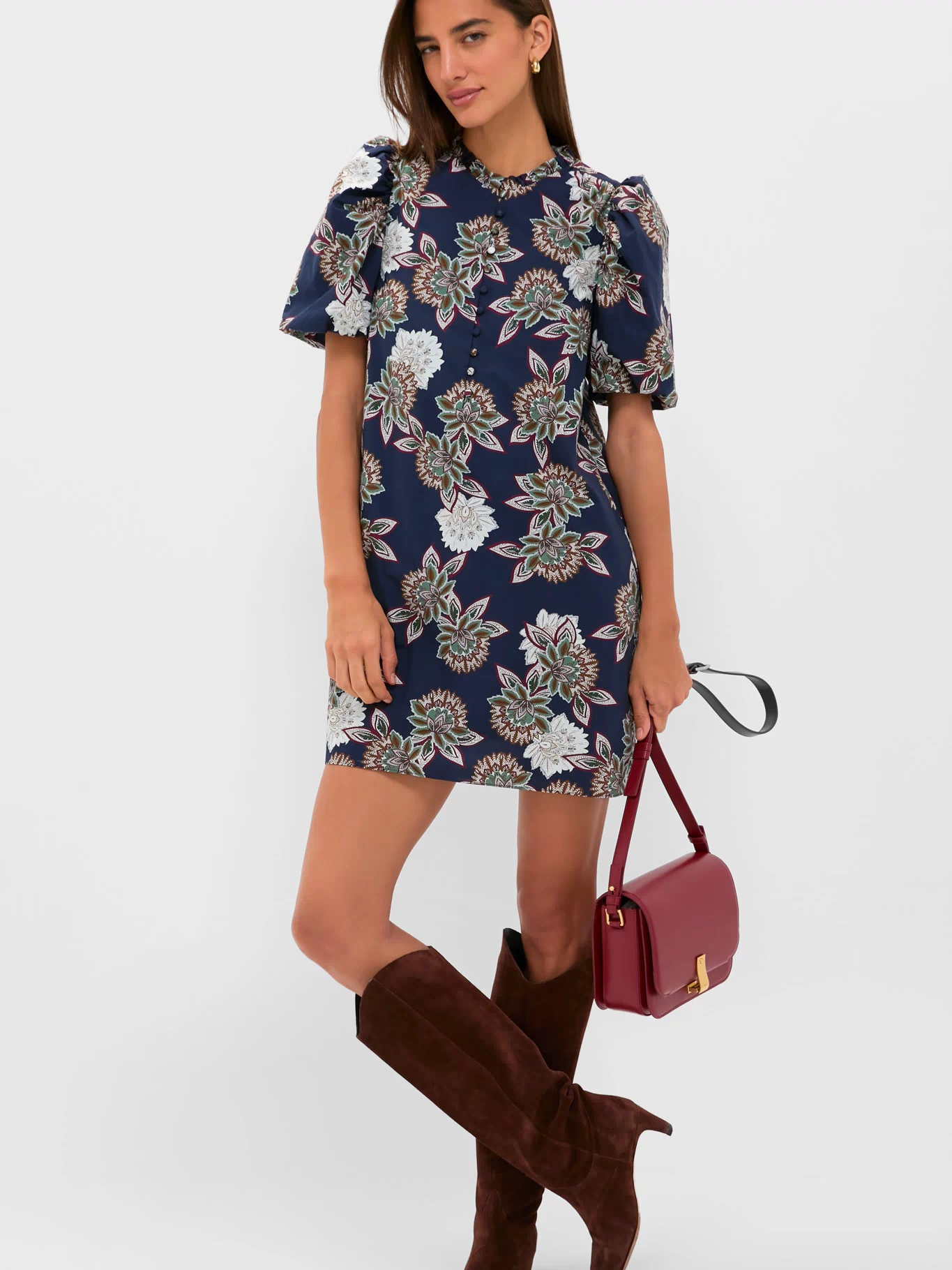 Model wearing the Navy Floral Mimi Mini Dress with classic puff sleeves and ruffle collar, paired effortlessly with dark brown knee-high boots and a burgundy crossbody bag.