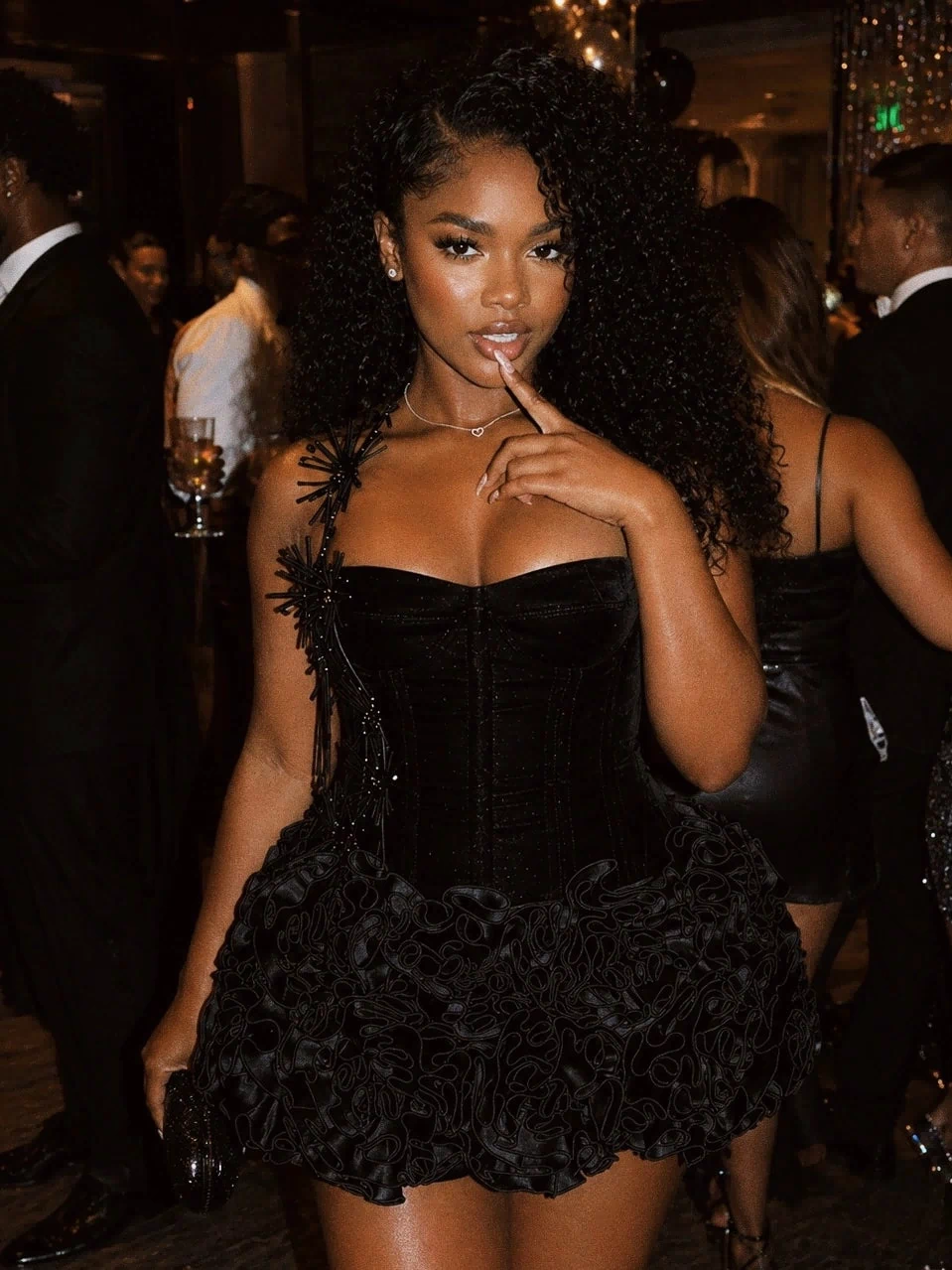 Woman in a black dress posing at an event with blurred background