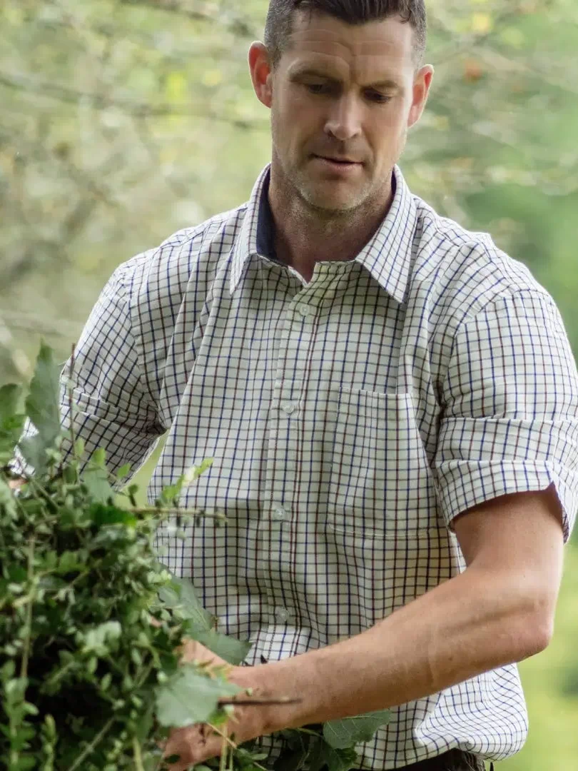 Man in a checkered shirt examining plants outdoors, showcasing a forest short sleeved style
