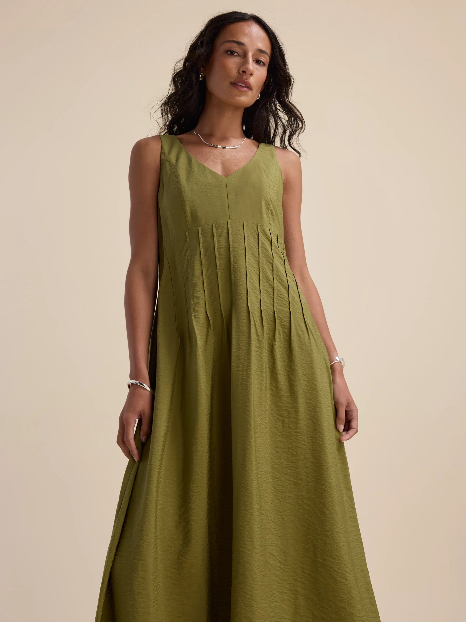 Woman in Max's Nina Fit and Flare Dress, sleeveless dill green, against a beige background.