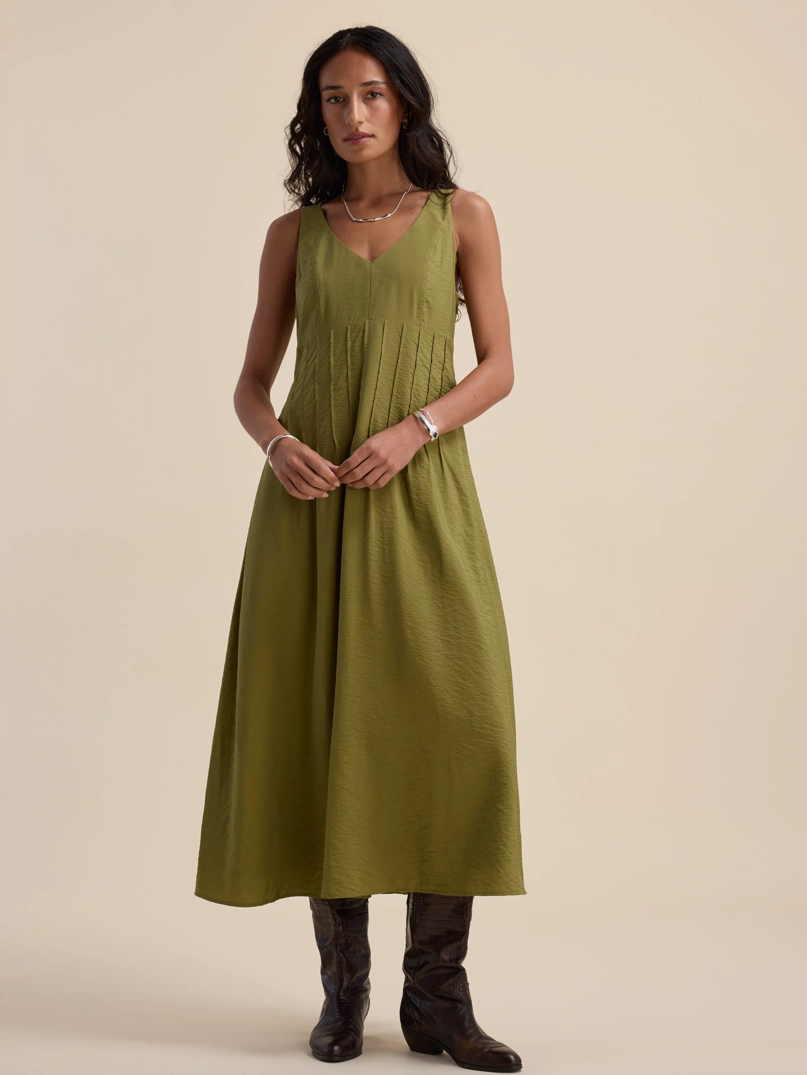Woman in the Max Nina Fit and Flare Dress, dill green, with dark boots against a beige background.