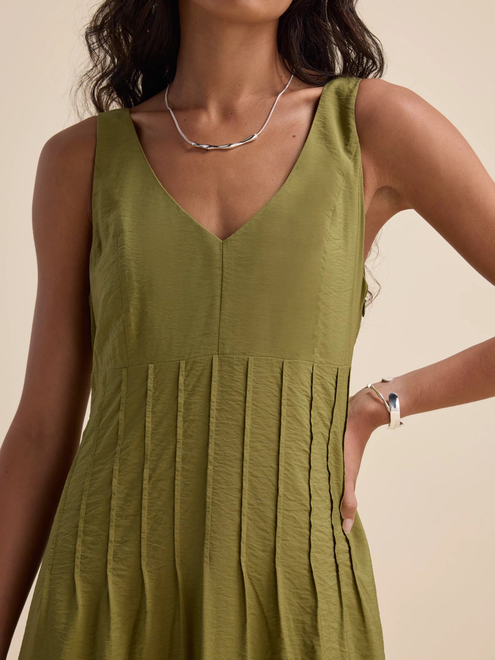 Woman wearing Max's Nina Fit and Flare Dress in dill green, with silver necklace and bracelet.