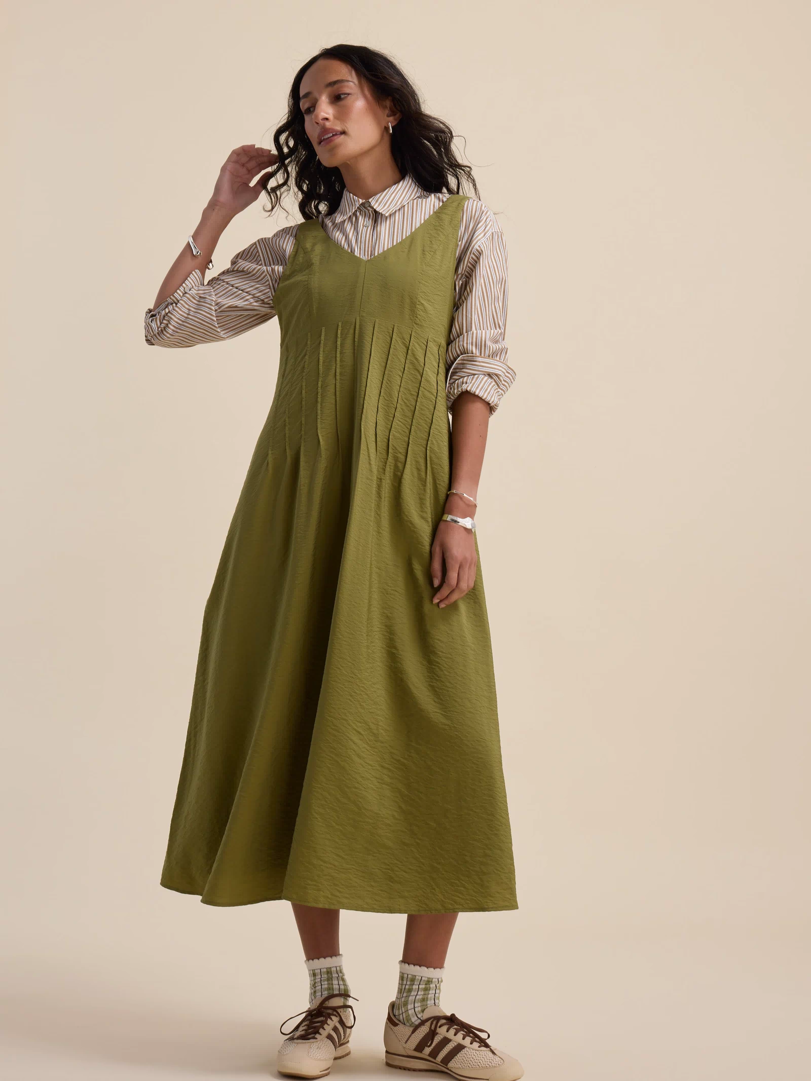 Woman in Max’s Nina Fit and Flare Dress in dill green over a striped shirt with socks and sneakers.