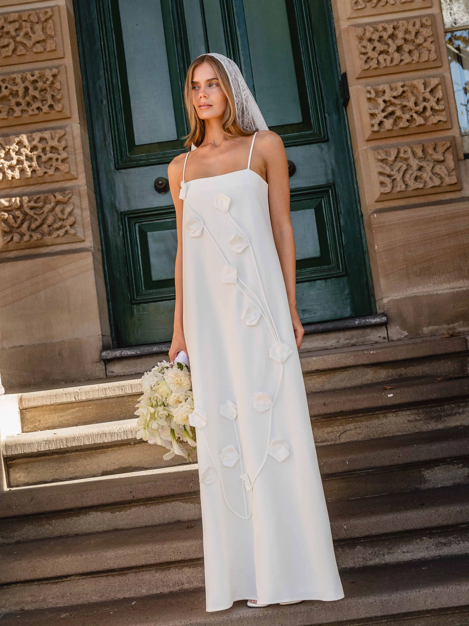 Brunette model wearing the Nolana Floral Applique Gown in White campaign shot