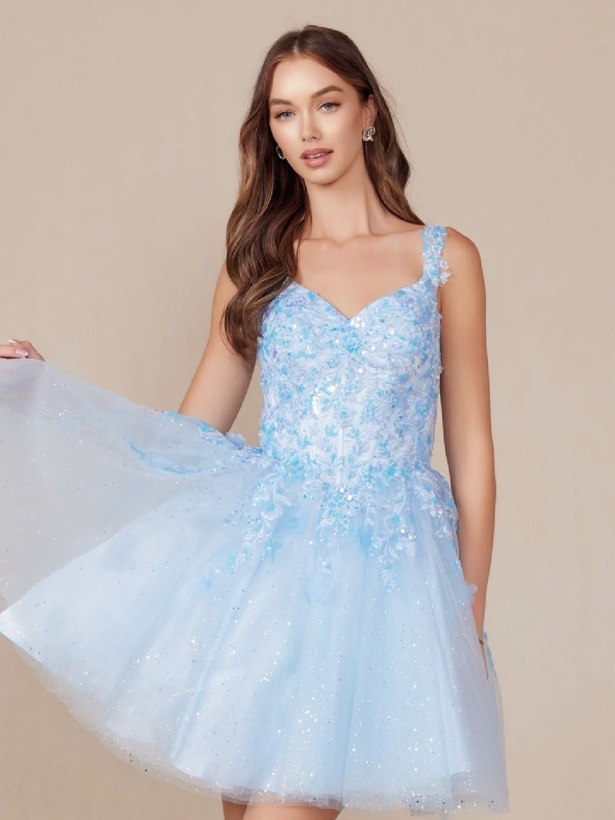 A woman in the Embroidered-Bodice Short A-Line Hoco Dress H846, featuring a light blue hue, floral embellished bodice, and tulle skirt, stands against a plain beige background.
