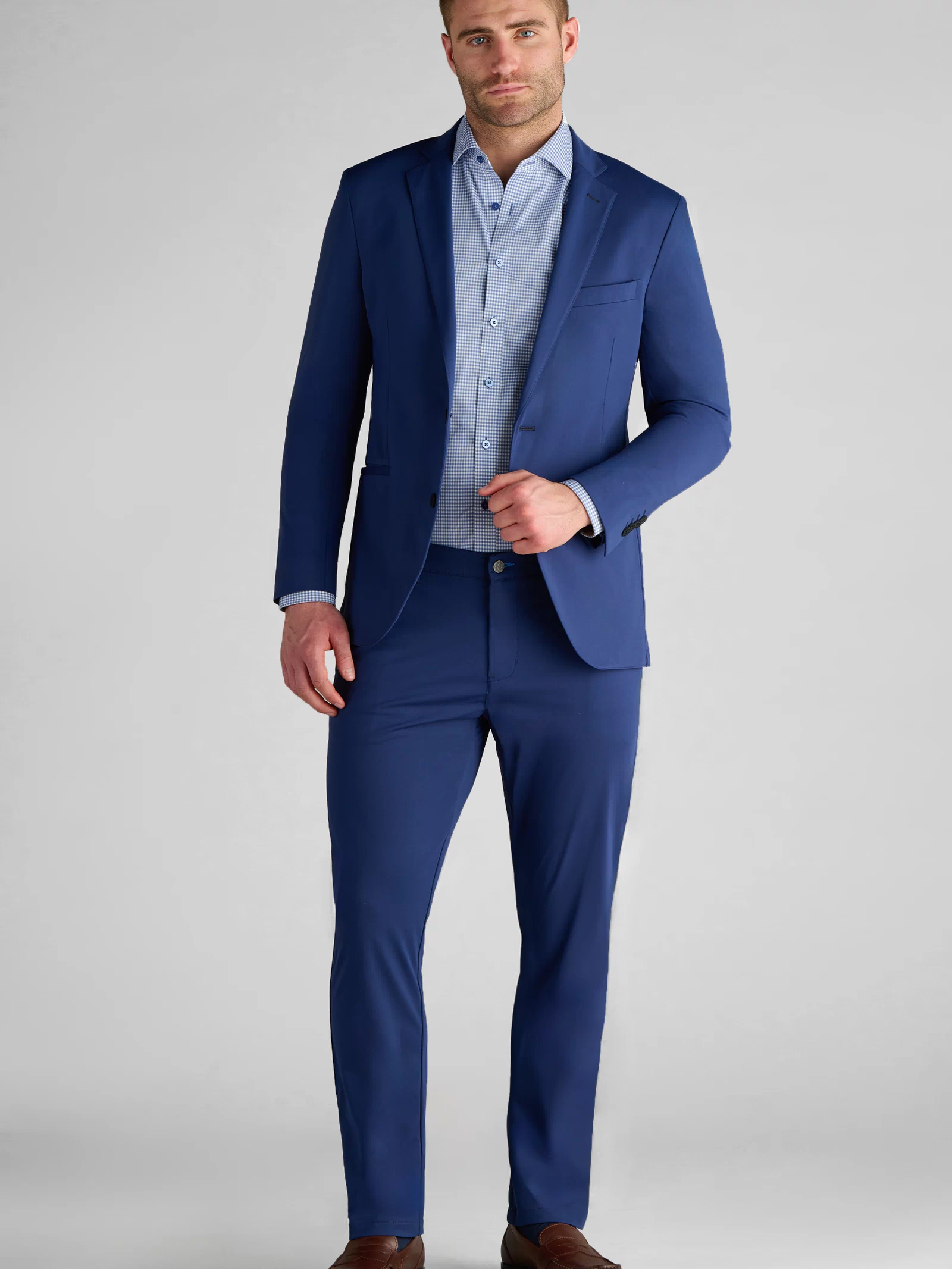 A man with short brown hair and a trimmed beard wears the Twillory Performance Blazer in Cobalt Blue with matching pants, a light blue shirt, and brown dress shoes, standing against a plain light gray background.