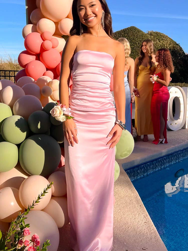 Full length view of a light pink satin strapless maxi dress with a ruched bodice and a flowing skirt