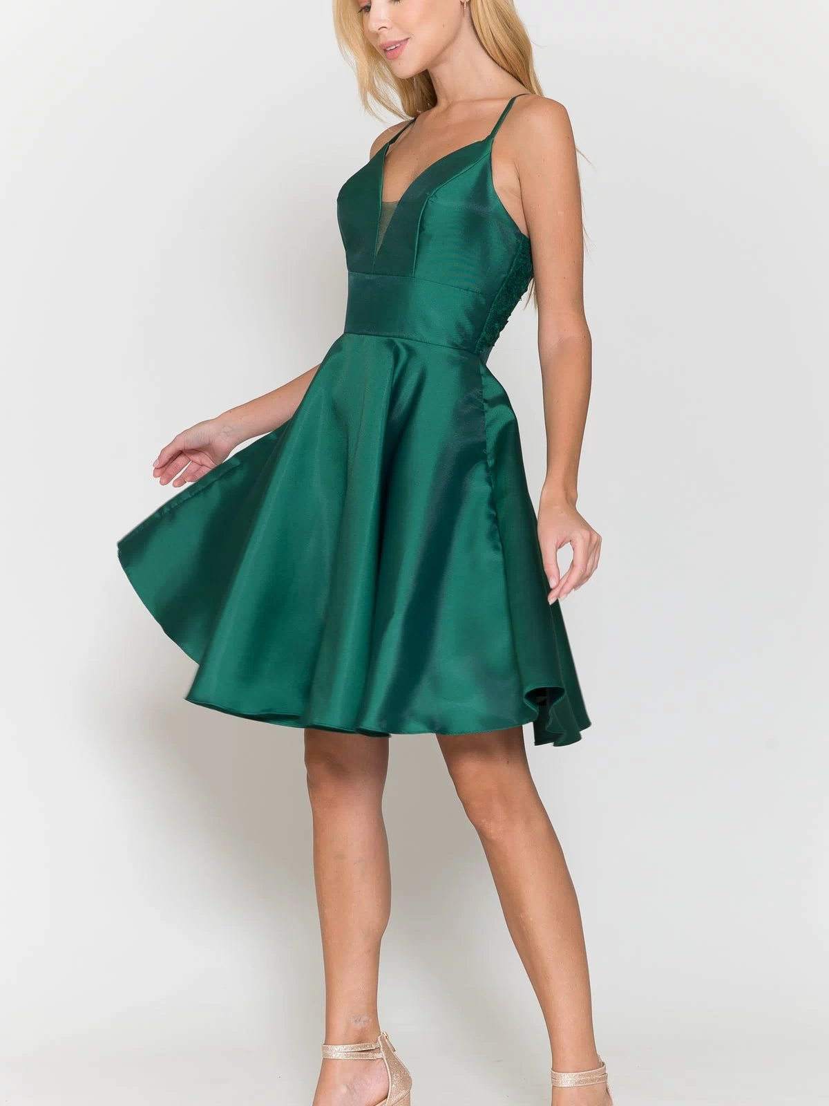 A woman in the Lace-Back Short A-Line Homecoming Dress 8698—sleeveless, deep green with a V-neck and knee-length hem—stands against a plain white background, paired with strappy heels.