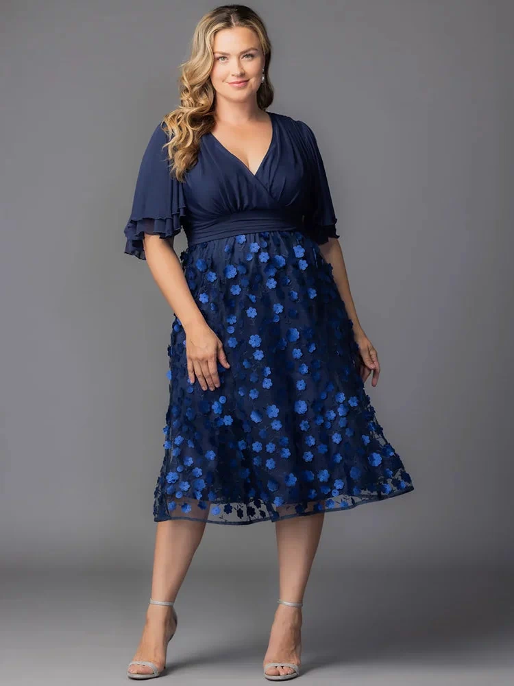 Pretty Petals Mesh Cocktail Dress in Navy Blooms. Model in a black and blue  floral cocktail dress posing in front of a grey background.