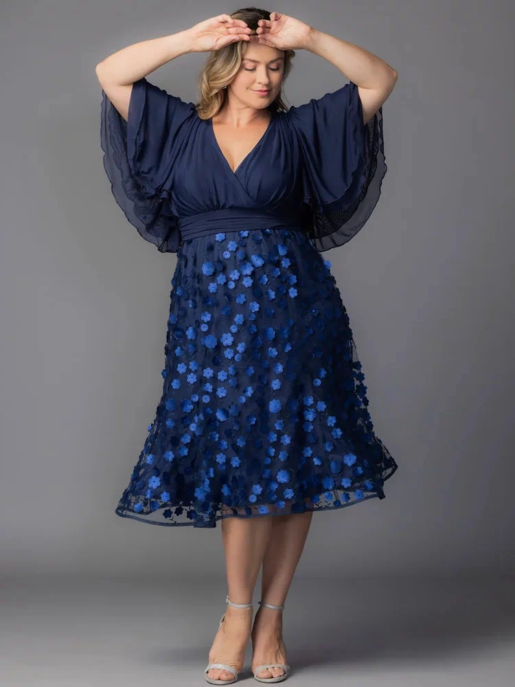 Pretty Petals Mesh Cocktail Dress in Navy Blooms. Model in a black and blue  floral cocktail dress posing in front of a grey background.