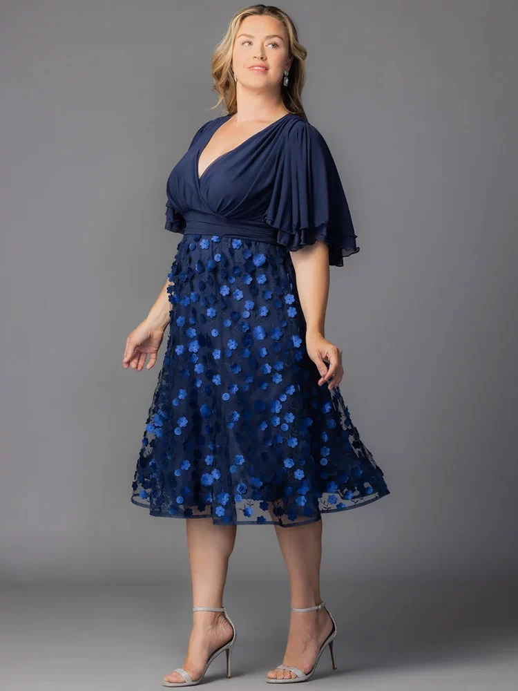 Pretty Petals Mesh Cocktail Dress in Navy Blooms. Model in a black and blue  floral cocktail dress posing in front of a grey background.
