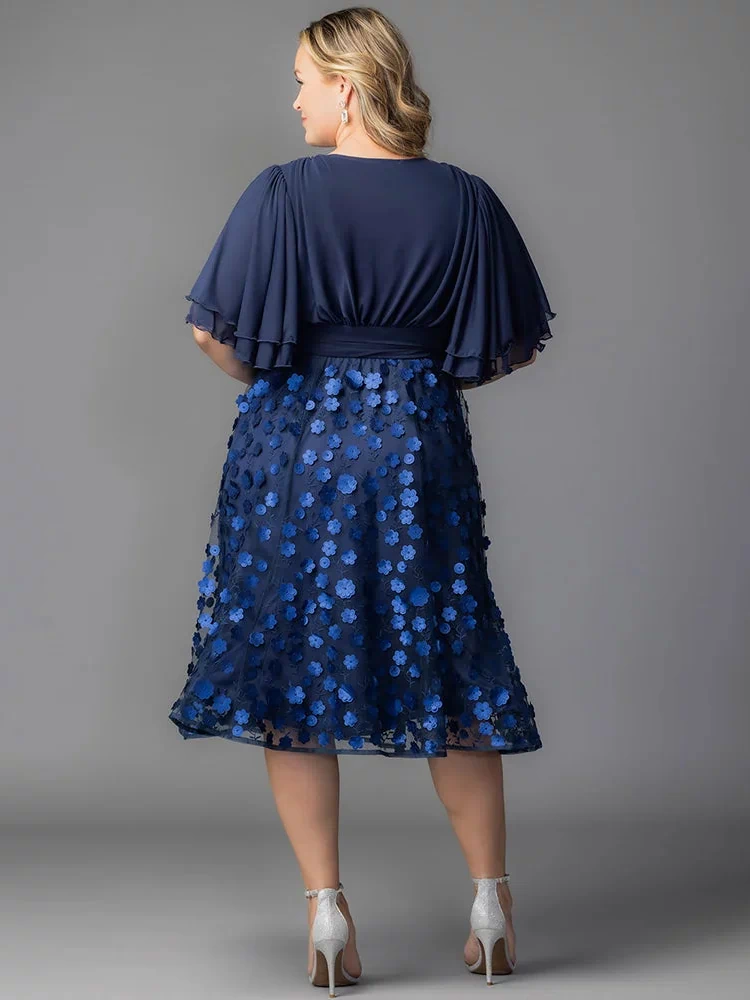 Pretty Petals Mesh Cocktail Dress in Navy Blooms. Model in a black and blue  floral cocktail dress posing in front of a grey background.