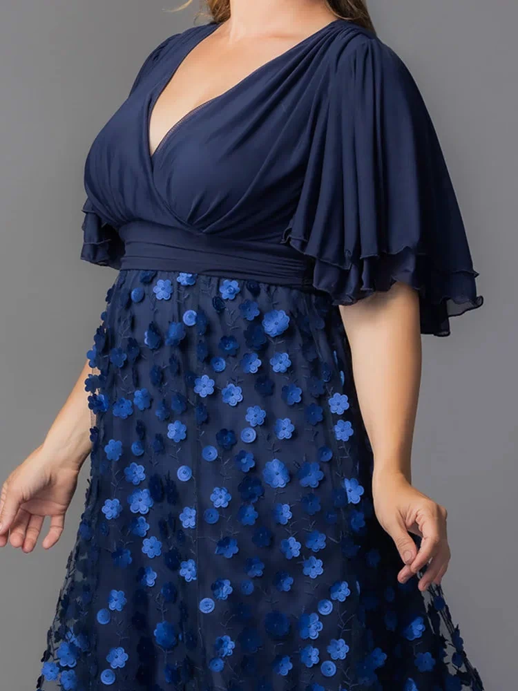 Pretty Petals Mesh Cocktail Dress in Navy Blooms. Model in a black and blue  floral cocktail dress posing in front of a grey background.