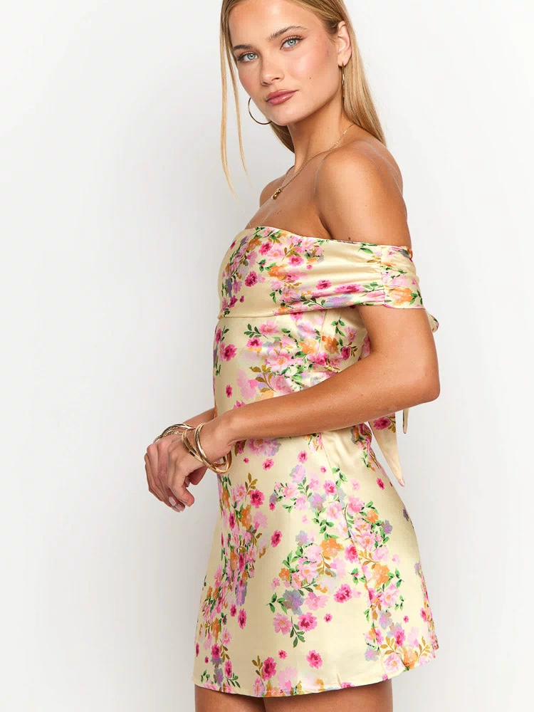 Side view of a primrose yellow floral mini dress with ruched off-shoulder sleeves and a side tie detail