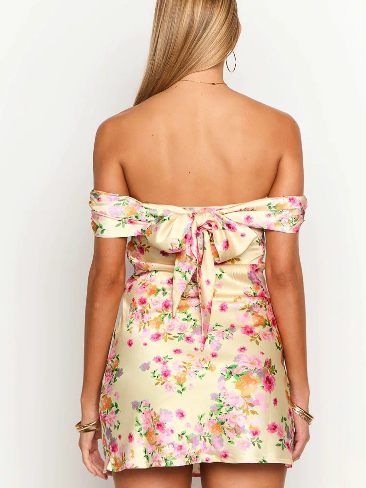 Back view of a primrose yellow floral off-the-shoulder mini dress with a large tie-back bow