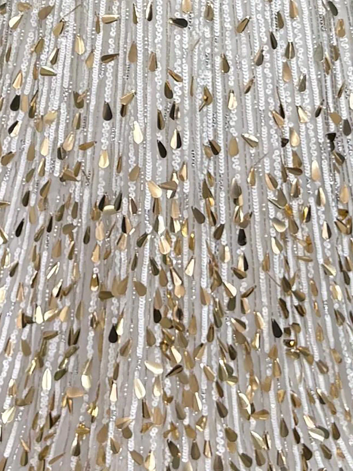 Close-up of the white fabric on the Sparkly Sequin Prom Dress: PromGirl Exclusive 250304, showing vertical sequin rows and metallic gold accents that create a shimmering, textured look.