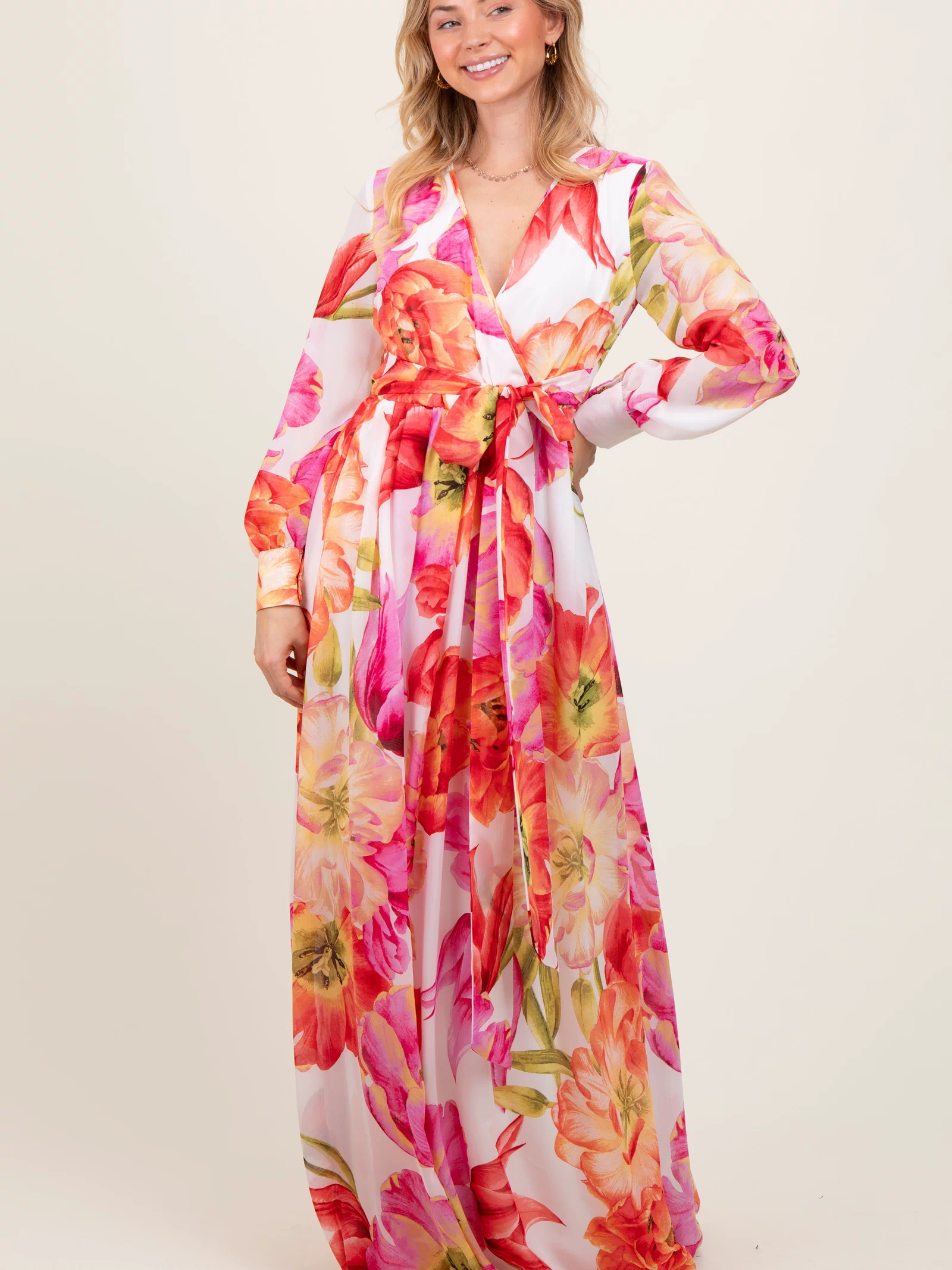 woman wearing a floral long sleeve maxi dress with pink and orange flowers and a tie waist detail