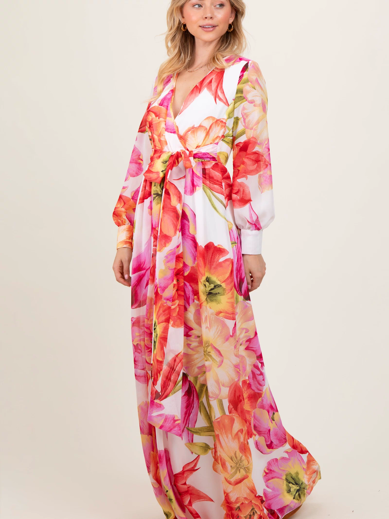 woman wearing a long floral dress with vibrant pink and orange flowers and a tie waist detail
