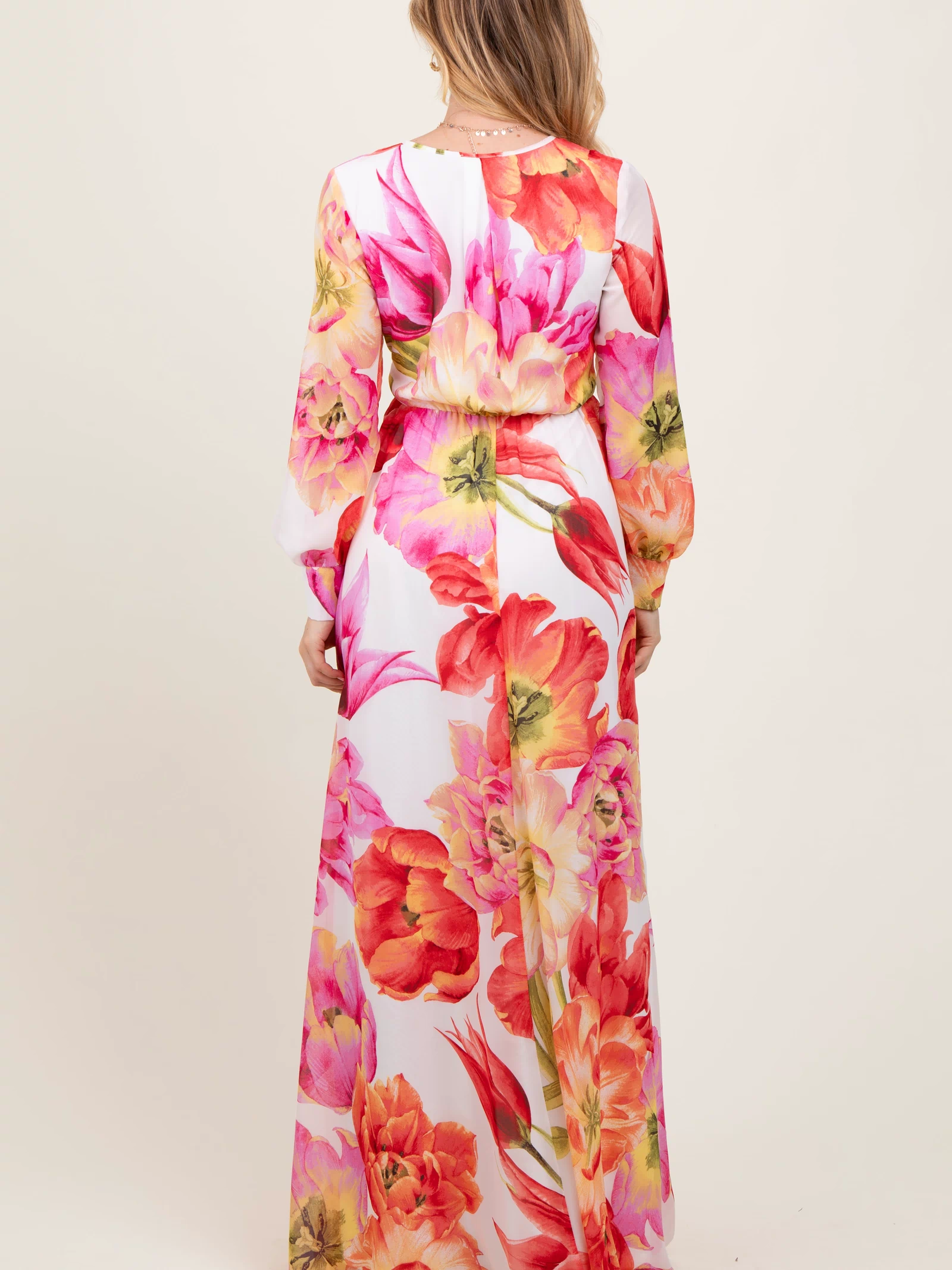 woman wearing a long floral maxi dress with a fitted waist and long sleeves, showing vibrant pink and orange flowers