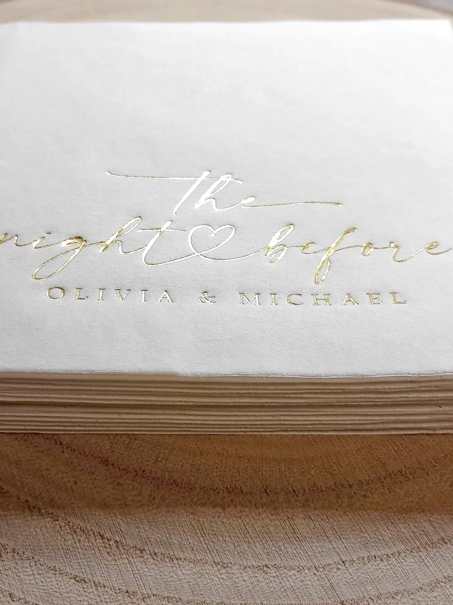 Stack of white napkins with gold text on a wooden surface