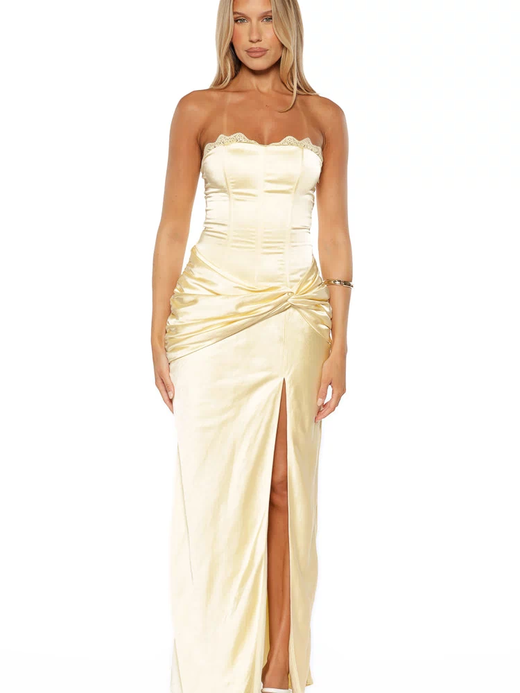 Front view of a yellow satin strapless maxi dress with lace trim neckline, corset bodice, ruched twist waist, and high split