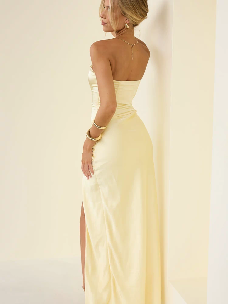 Side view of a yellow strapless satin maxi dress with ruched detailing on the hip and a high side slit