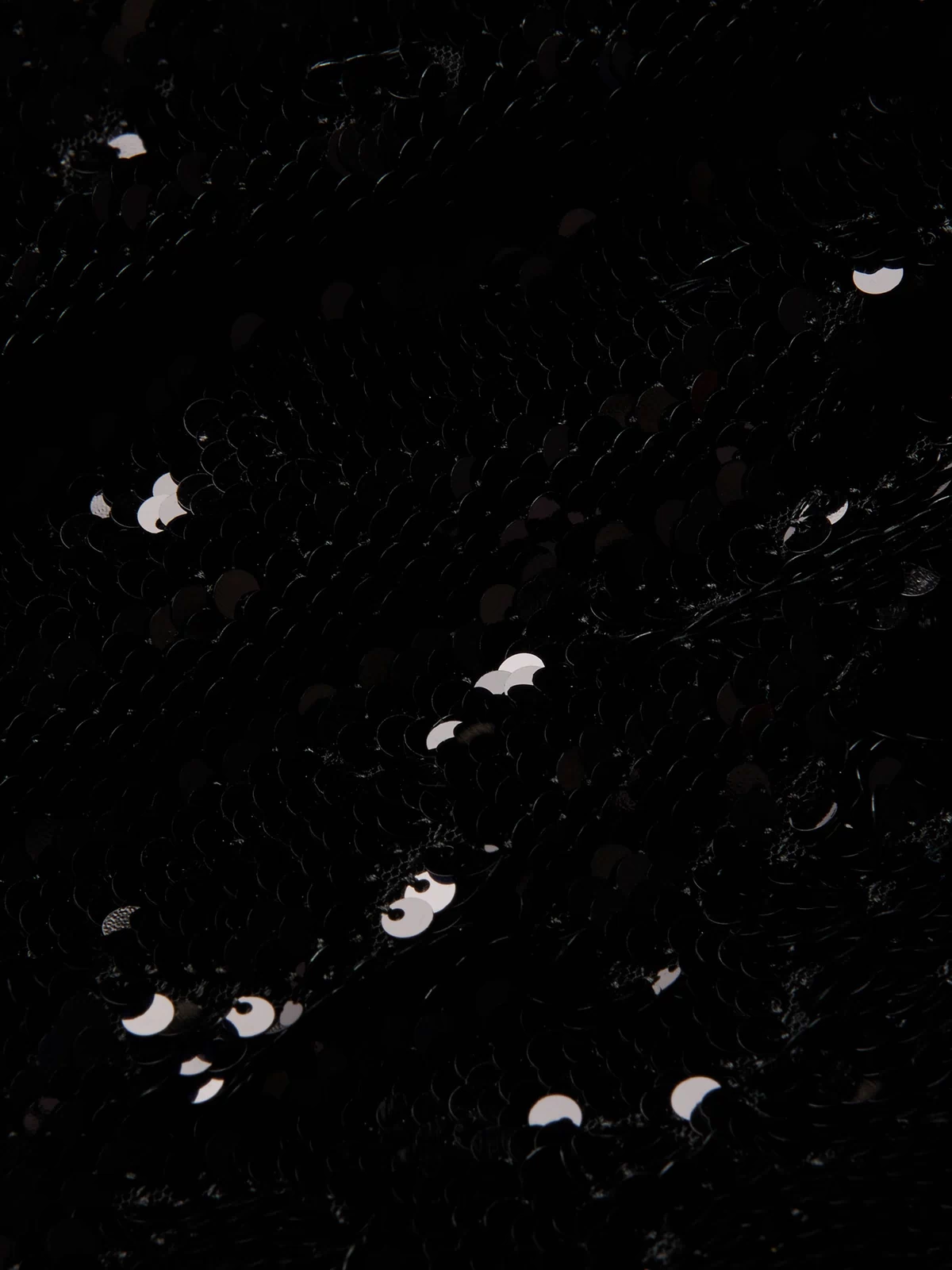 Close-up of black fabric on the Sayla Sequin Gown, covered with shiny black sequins reflecting small spots of light, creating a textured and sparkling effect reminiscent of vintage glamour.