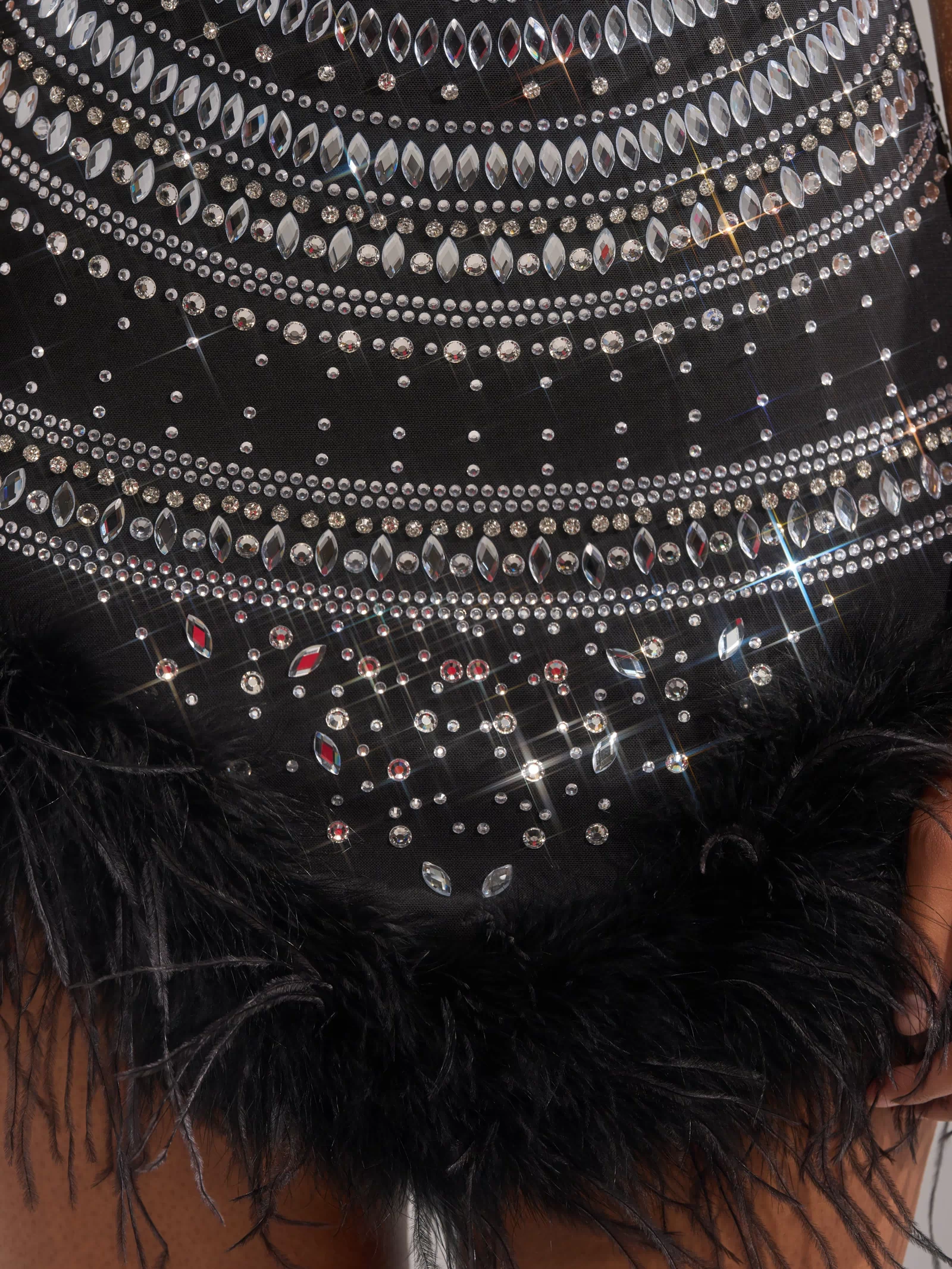 A close-up of the SHOWSTOPPER RHINESTONE MINI DRESS, a bodycon LBD adorned with silver rhinestones and sequins, featuring a black feather-trimmed hem. Two hands by the sides highlight this chic feather trim dress.
