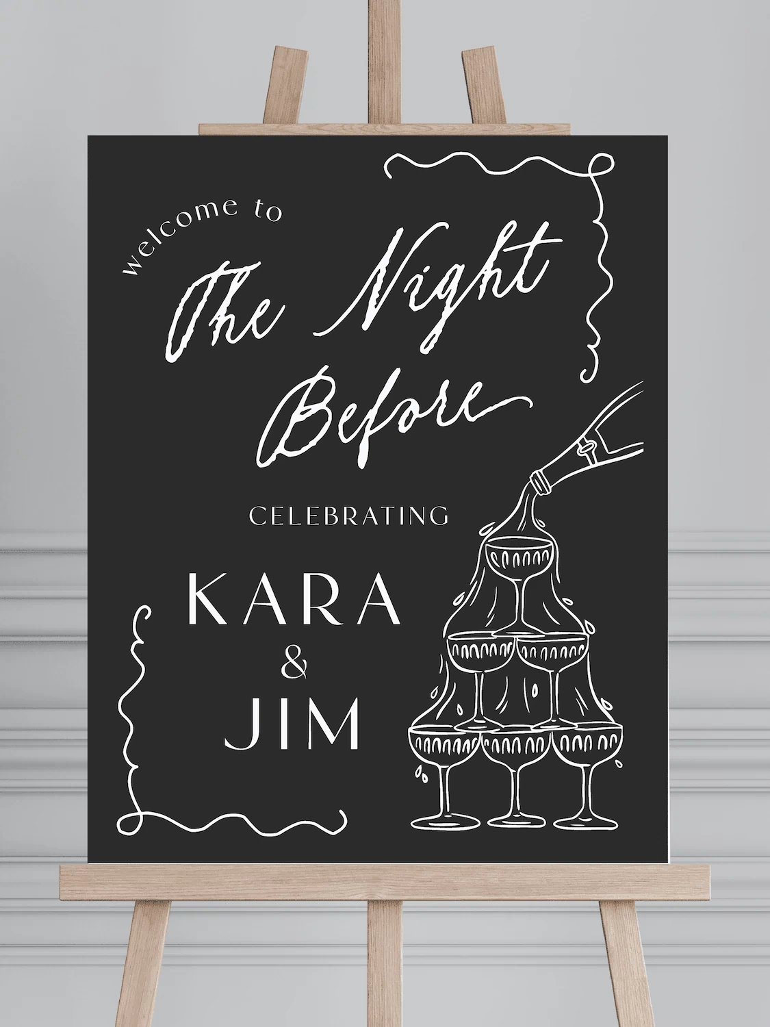 Black welcome sign with white script reading "The Night Before" and champagne tower design, personalized with "Kara & Jim" names