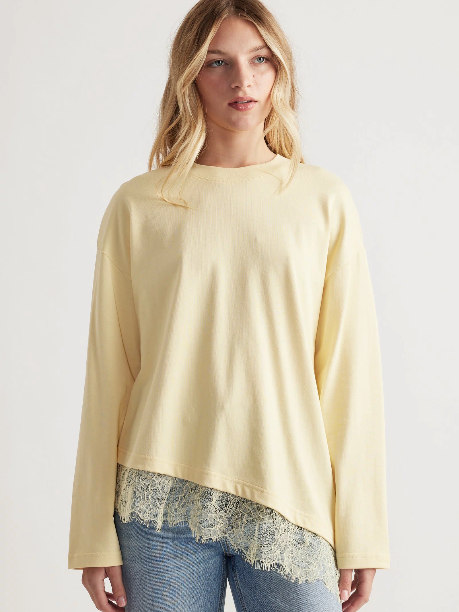 Woman wearing a soft yellow long-sleeve top with lace trim hem paired with light wash denim jeans