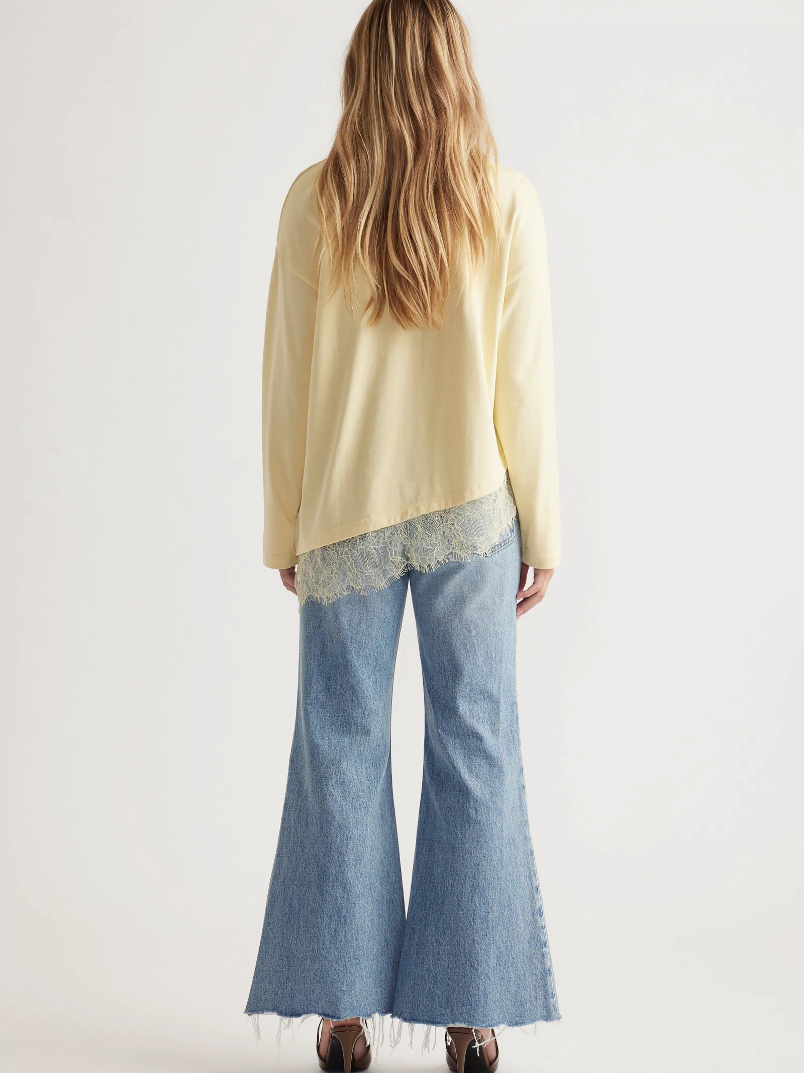 Woman wearing a pale yellow long sleeve top with lace trim paired with light blue wide-leg raw-hem jeans and heels