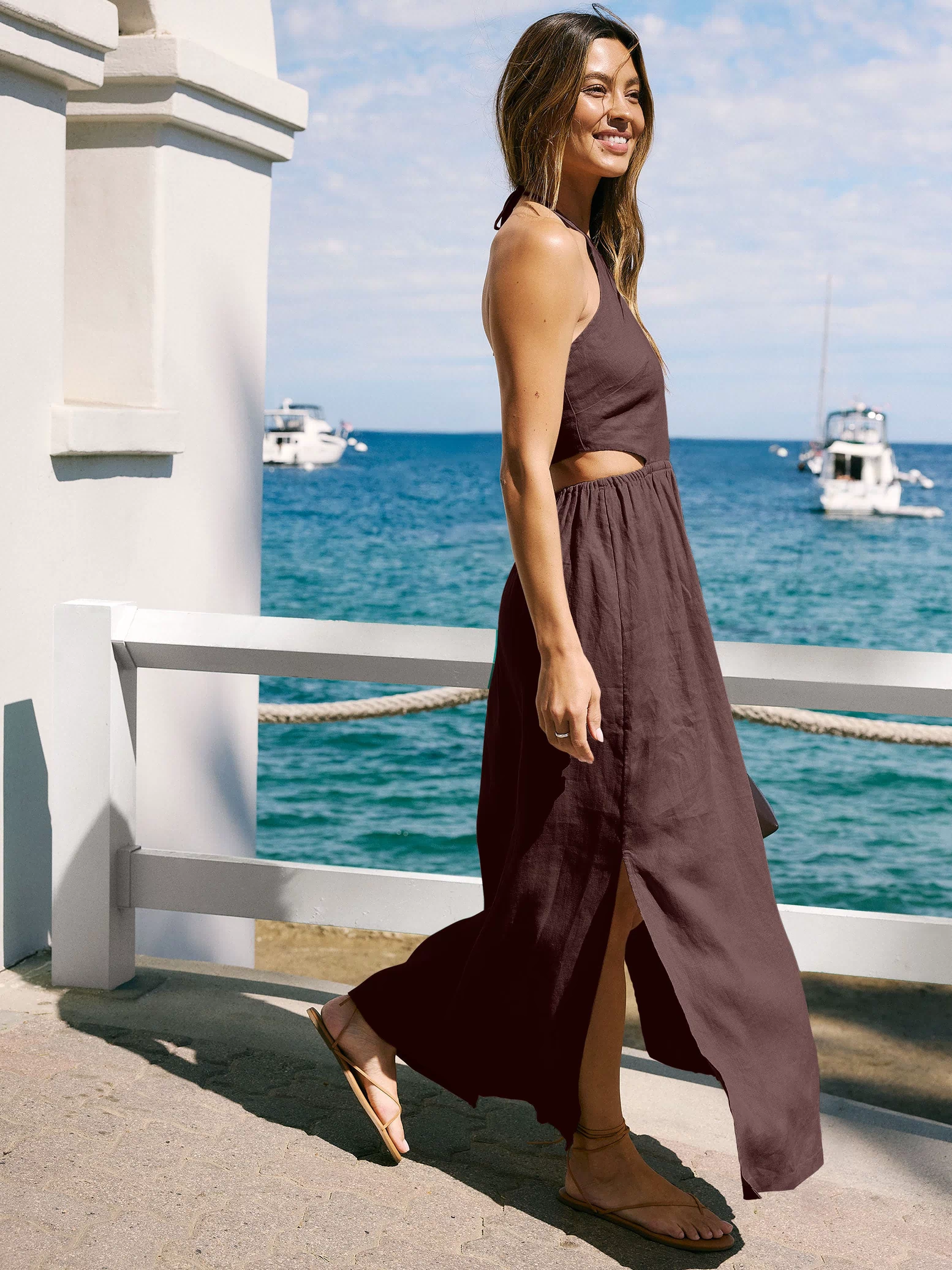 Woman in a brown linen halter dress standing against a white wall with ocean view. 