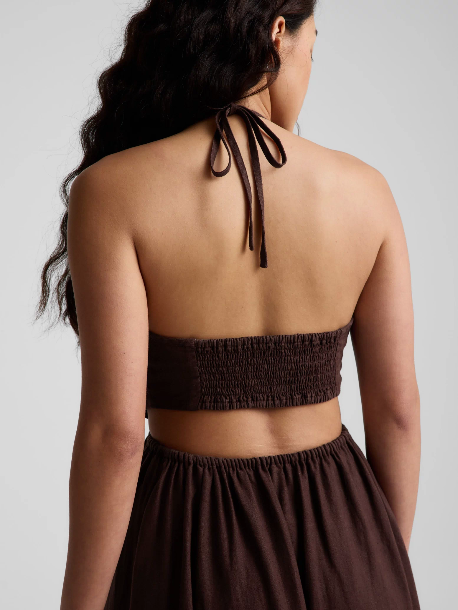 Woman wearing a brown halter neck midi dress on a plain background. 