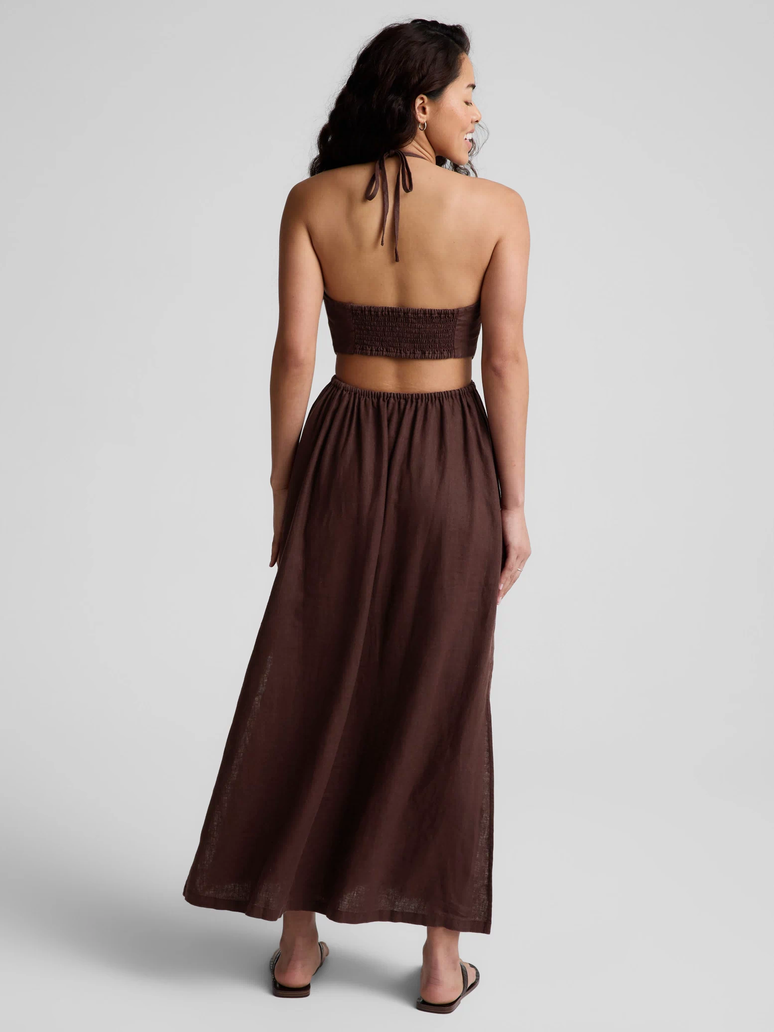 Woman wearing a brown halter neck midi dress on a plain background. 